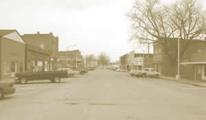 Sepia toned picture of town with cars parked along the sides.